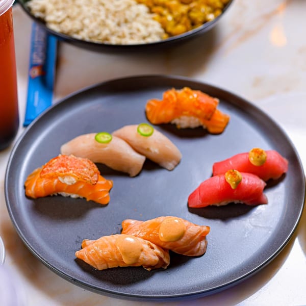 A dark plate holds various Sweetfish Poké Bowls & Sushi nigiri, including salmon, tuna, and white fish.