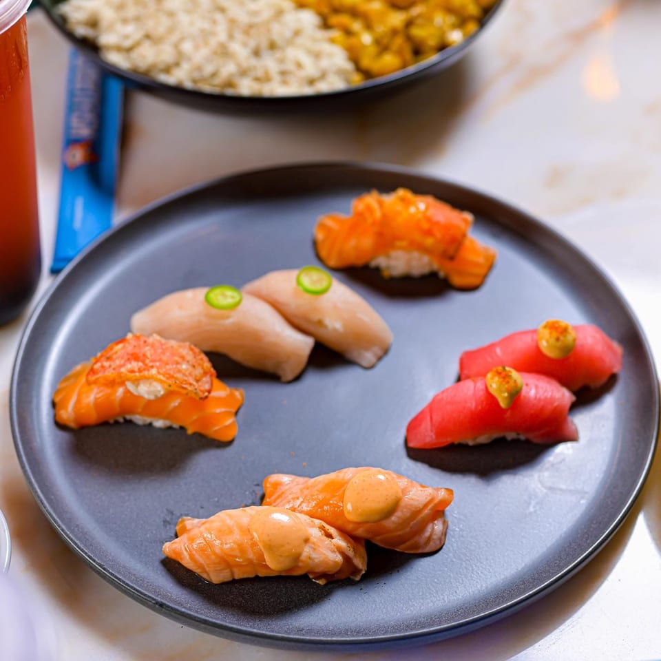 A dark plate holds various Sweetfish Poké Bowls & Sushi nigiri, including salmon, tuna, and white fish.