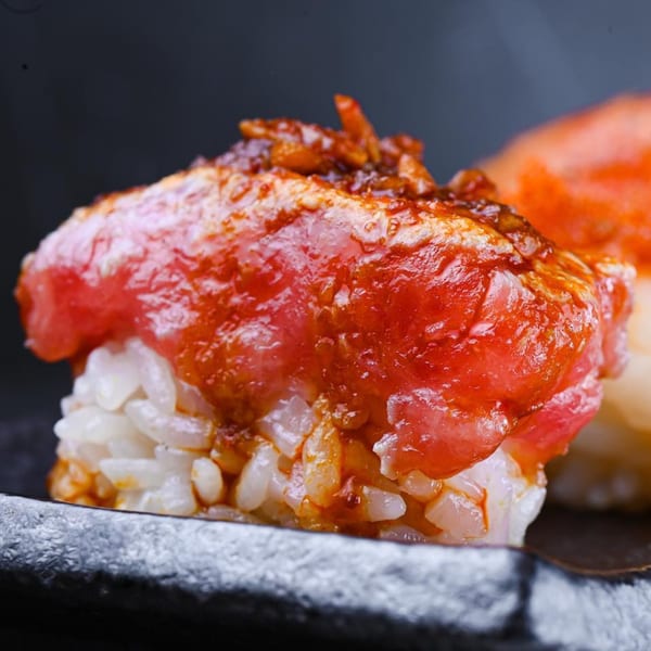 Close-up of a Sweetfish sushi piece with red fish and a spicy topping on white rice.