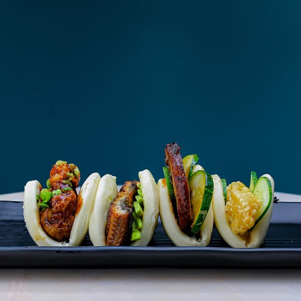 Four Sweetfish Poké Bowls & Sushi bao buns with various fillings on a black plate.