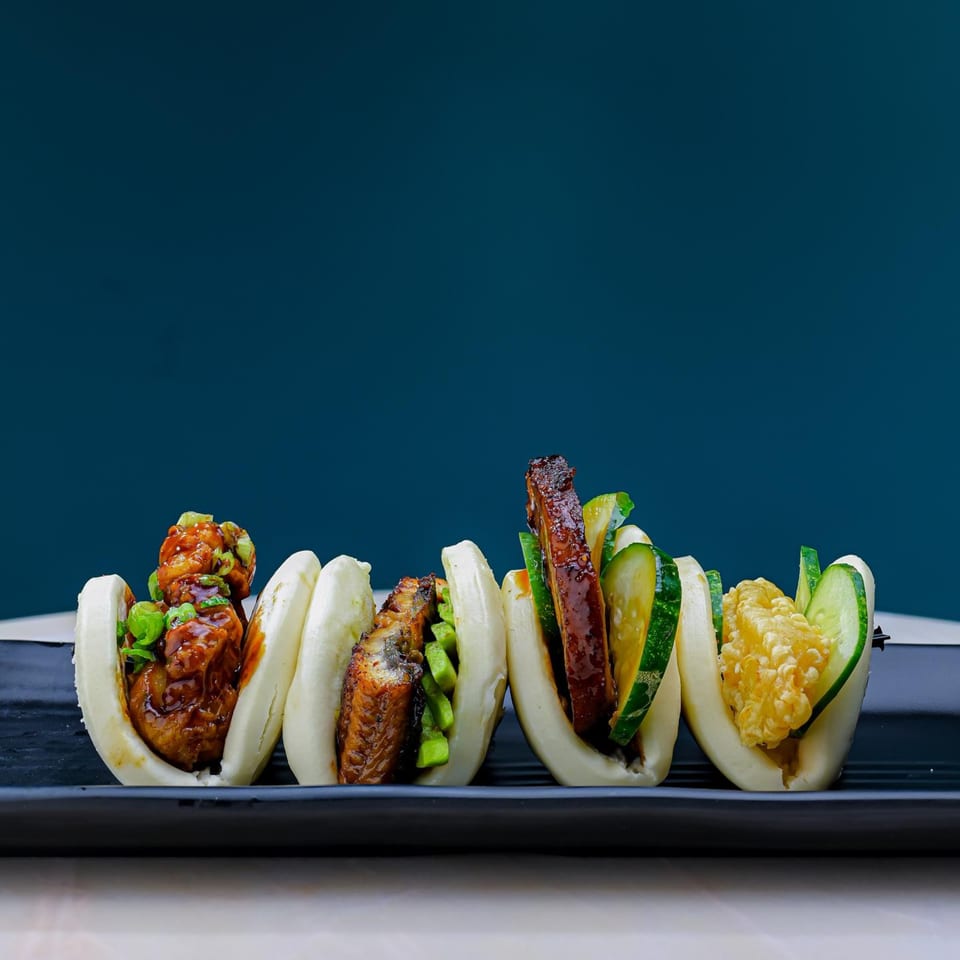 Four Sweetfish Poké Bowls & Sushi bao buns with various fillings on a black plate.