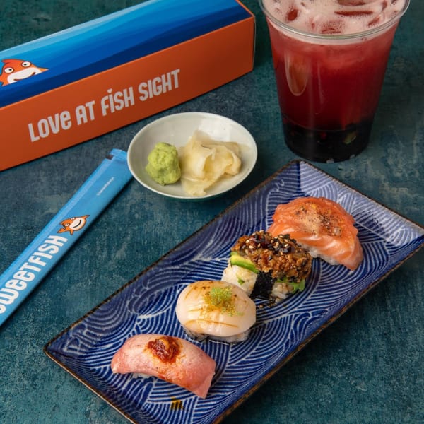 Sweetfish sushi platter with various nigiri and rolls, wasabi, ginger, a drink, and branded box.