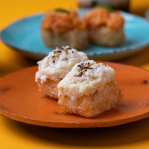 Two Sweetfish sushi pieces with white topping and sesame seeds on an orange plate.