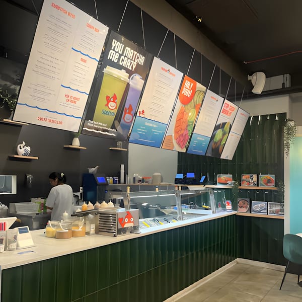 A Sweetfish Poké Bowls & Sushi restaurant interior with a counter, menu boards, and a staff member.