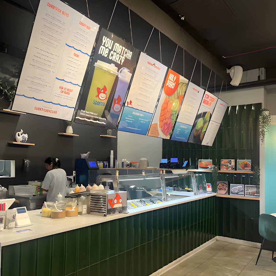 A Sweetfish Poké Bowls & Sushi restaurant interior with a counter, menu boards, and a staff member.