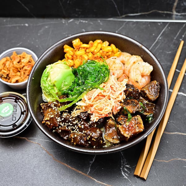 Sweetfish Poké Bowl with shrimp, avocado, seaweed, corn, and beef on a dark marble surface.