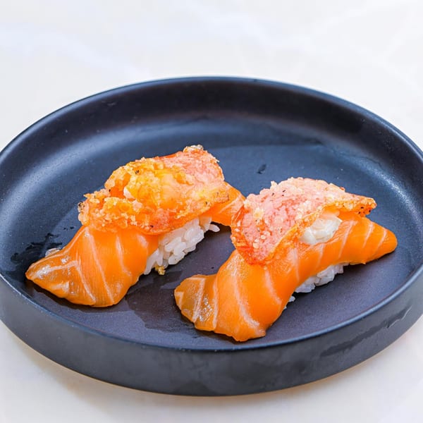 Two pieces of Sweetfish salmon nigiri sushi with crispy topping on a dark plate.